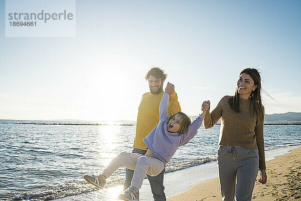 Glückliche Eltern spielen mit ihrer Tochter am Strand