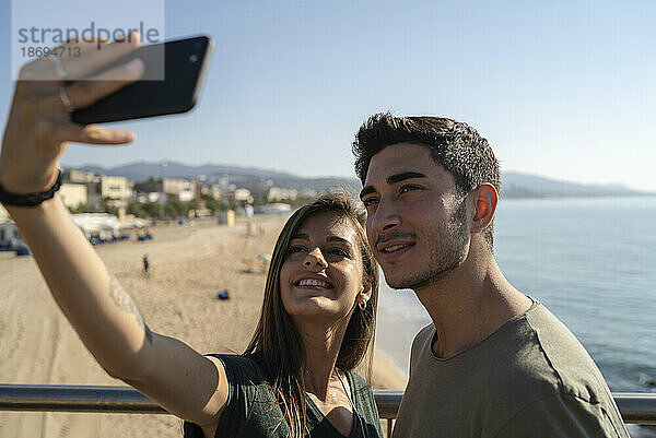 Lächelnde junge Frau macht ein Selfie mit ihrem Freund per Smartphone