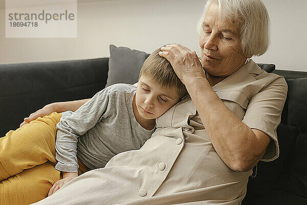 Junge entspannt sich bei Großmutter  die zu Hause auf dem Sofa sitzt