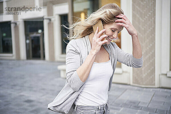 Blonde Frau mit der Hand im Haar telefoniert