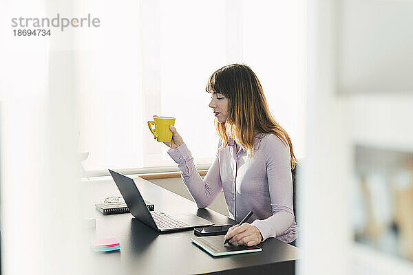Geschäftsfrau mit Kaffeetasse sitzt am Schreibtisch