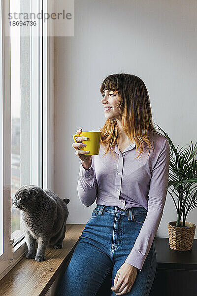 Lächelnde Geschäftsfrau mit Kaffeetasse am Fenster sitzend
