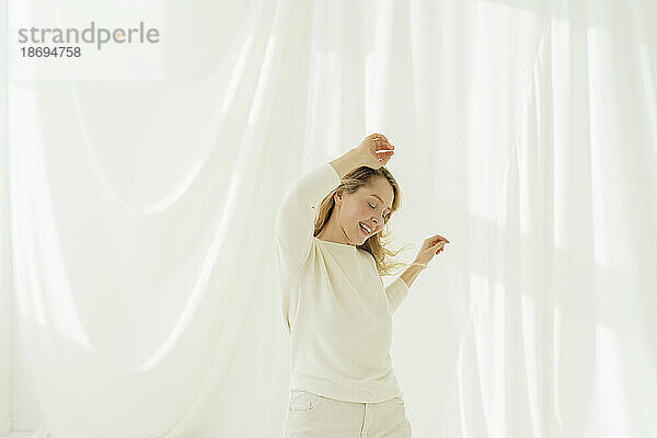 Frau mit geschlossenen Augen tanzt vor einem weißen  durchscheinenden Vorhang