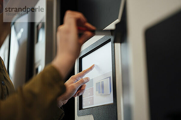 Frau berührt den Bildschirm eines Geldautomaten