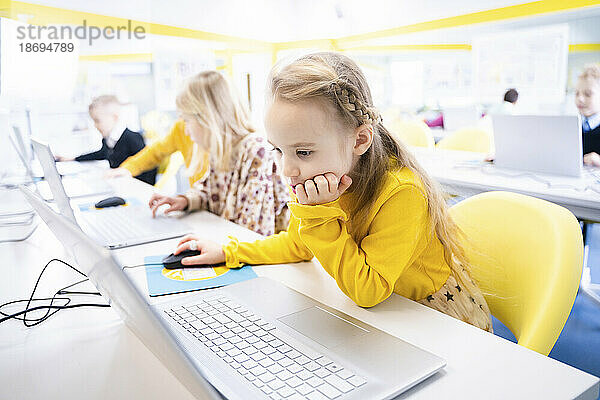 Blond schoolgirl learning through laptop in computer class