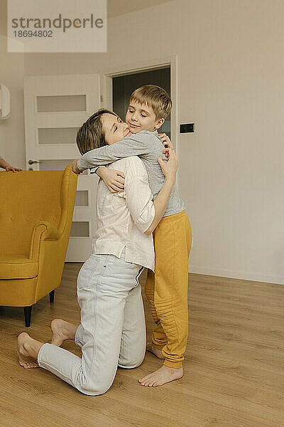 Junge umarmt Mutter  die zu Hause kniet