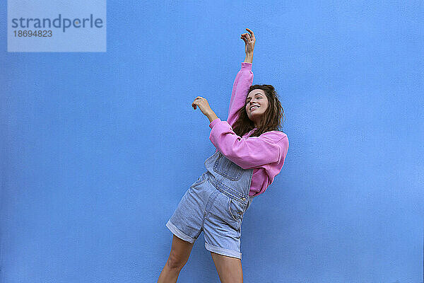 Carefree woman dancing against blue background