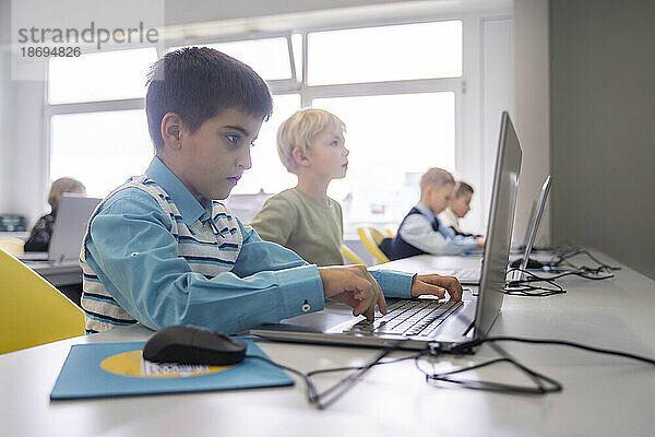 Boy doing E-learning through laptop sitting at desk in school