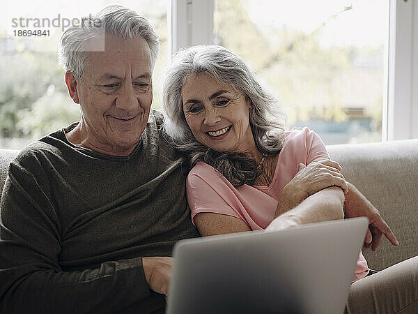 Glückliches älteres Paar mit Laptop  das es sich zu Hause auf der Couch gemütlich macht