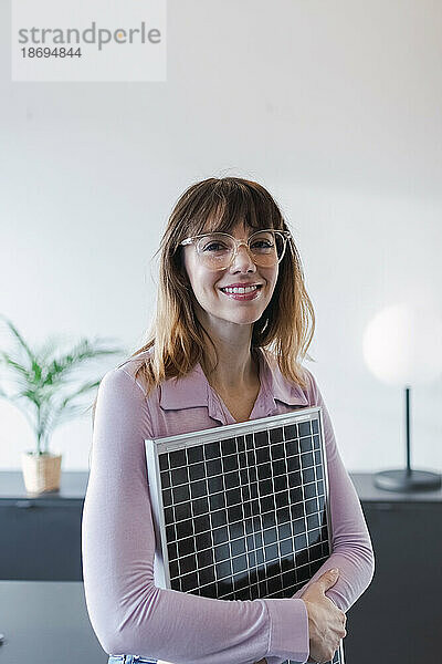 Lächelnde Geschäftsfrau hält Solarpanel im Büro