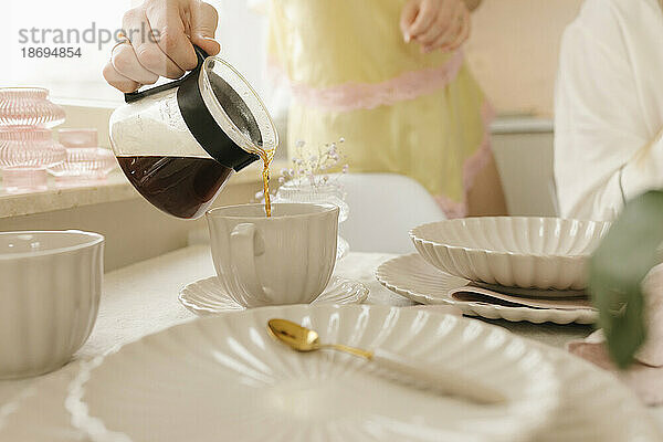 Frau gießt am Tisch zu Hause Kaffee in eine Tasse