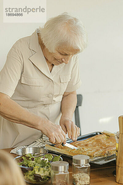 Elderly woman cutting cake at home