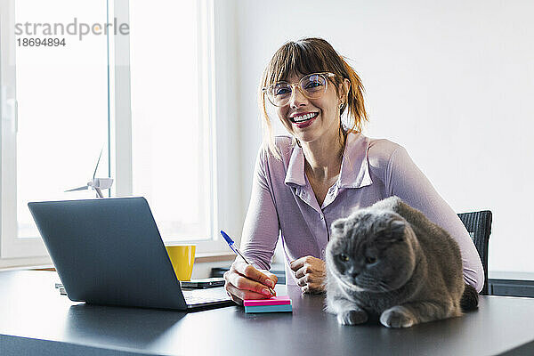Glückliche Geschäftsfrau mit Katze am Schreibtisch