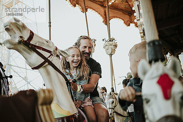 Glückliches Mädchen genießt Karussellfahrt mit Vater im Vergnügungspark