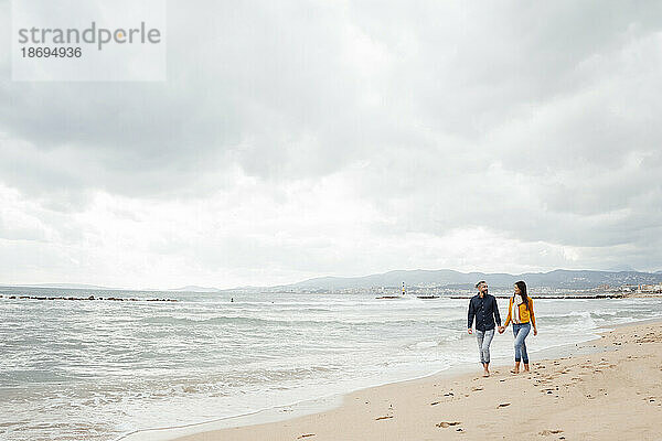 Mann und Frau gehen gemeinsam an der Küste am Strand spazieren