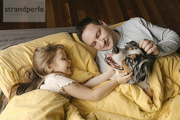 Vater und Tochter streicheln Hund  der zu Hause im Bett liegt
