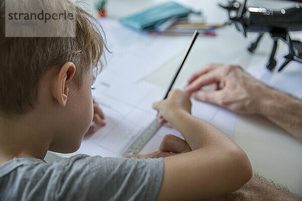 Vater hilft Sohn beim Zeichnen auf Papier am Schreibtisch