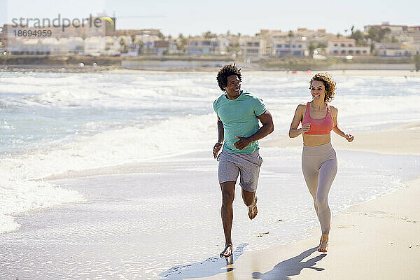 Lächelndes Paar joggt gemeinsam am Strand