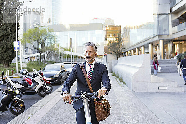 Geschäftsmann fährt mit Elektroroller auf Gehweg