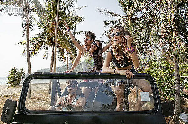 Fröhliche Freunde genießen die Fahrt mit dem Geländewagen am Strand