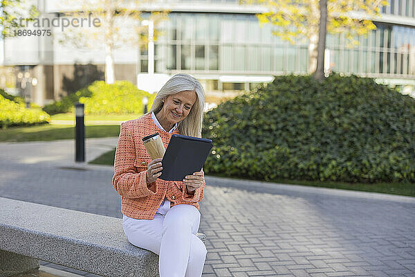 Lächelnde Geschäftsfrau  die auf einer Bank sitzt und einen Videoanruf über einen Tablet-PC tätigt