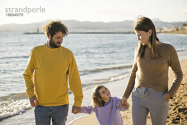 Vater und Mutter gehen mit Tochter am Strand spazieren