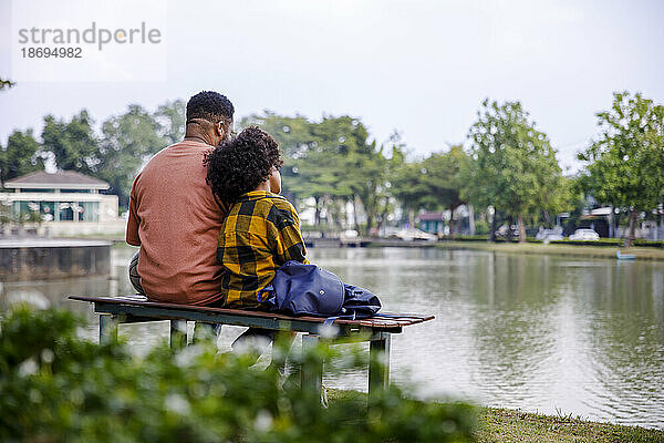 Father and daughter looking at pond sitting on bench