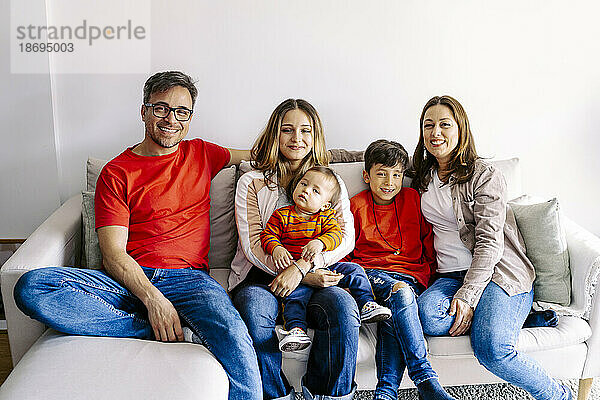 Lächelnde Familie sitzt mit Kindern zu Hause auf dem Sofa