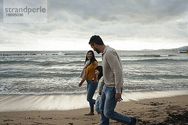 Glückliche Frau und Mann gehen mit Tochter am Strand spazieren
