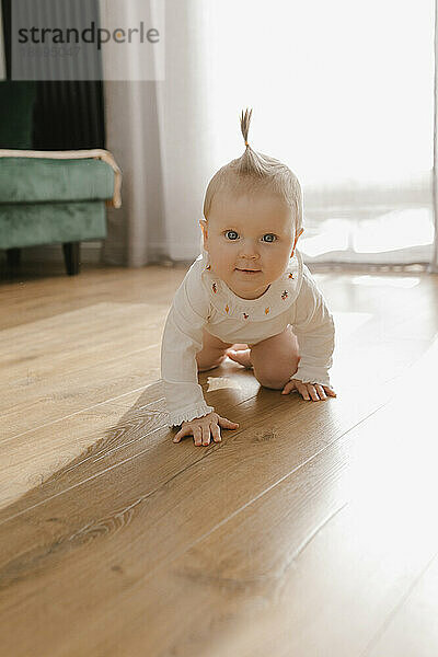 Süßes kleines Mädchen krabbelt zu Hause auf Hartholzboden