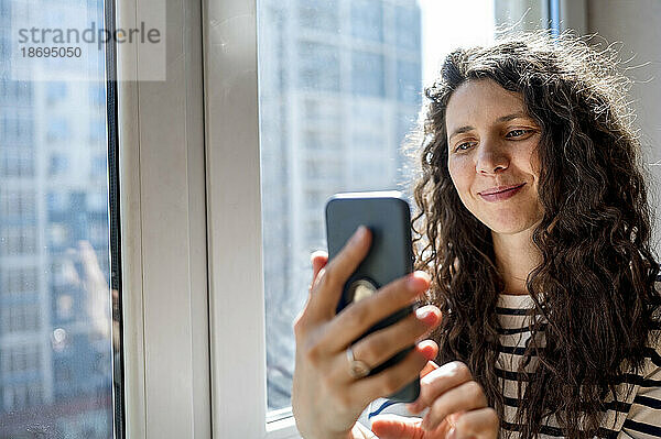 Lächelnde Frau benutzt Smartphone am Fenster