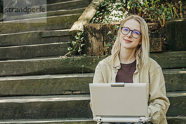 Lächelnde Geschäftsfrau mit Laptop sitzt auf Stufen