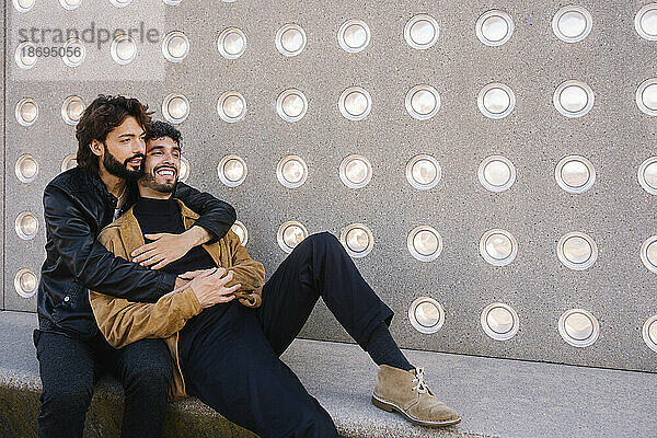 Gay couple sitting near concrete wall