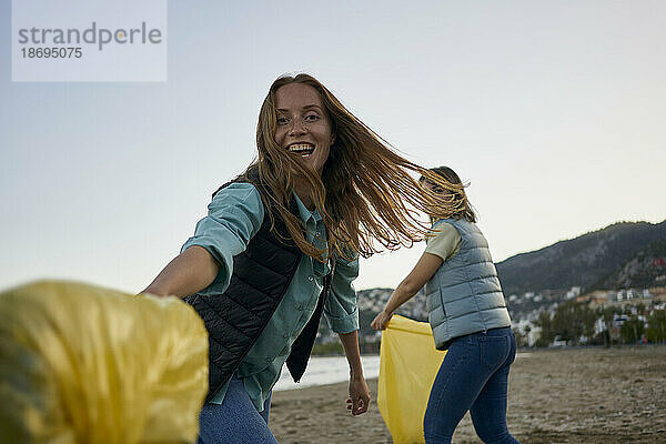 Fröhliche Freiwillige haben Spaß daran  Müllsäcke am Strand zu halten