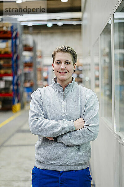 Confident young employee standing with arms crossed at factory