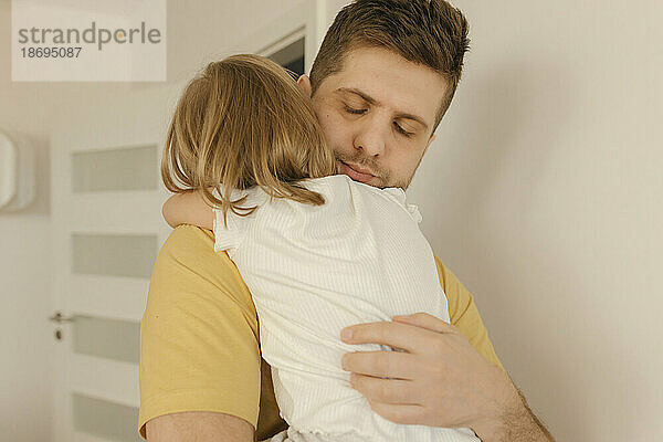 Vater mit geschlossenen Augen umarmt Tochter zu Hause