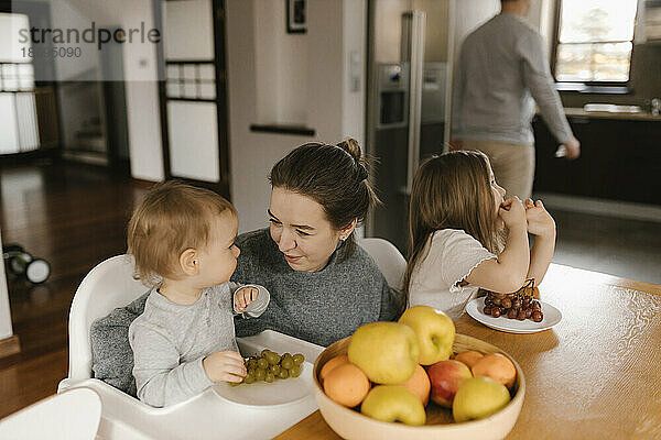 Mutter mit Kindern isst Obst am Esstisch