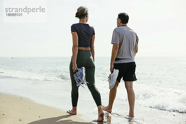 Paar mit Sportschuhen spaziert in Ufernähe am Strand