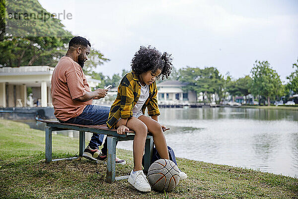 Mädchen mit Basketball sitzt auf der Bank ihres Vaters im Park