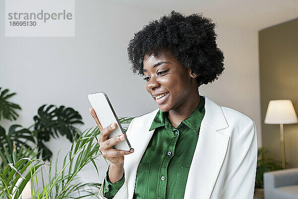 Lächelnde junge Geschäftsfrau  die im Büro ihr Smartphone benutzt