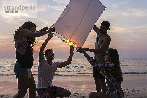 Freunde brennen Papierlaterne am Strand bei Sonnenuntergang
