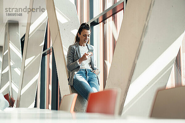 Geschäftsfrau benutzt Smartphone und stützt sich im Büro auf eine Säule