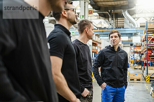 Mitarbeiter mit Händen in den Taschen diskutieren bei einer Besprechung in der Fabrik