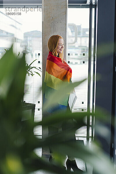 Junge Frau mit Regenbogenfahne am Fenster