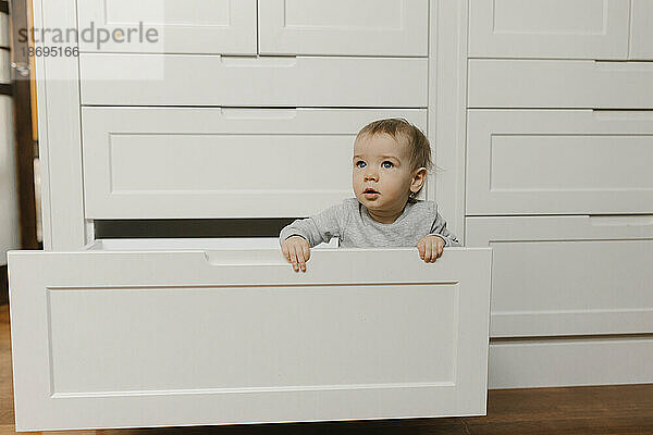 Kleiner Junge sitzt zu Hause in der Schublade des Kleiderschranks