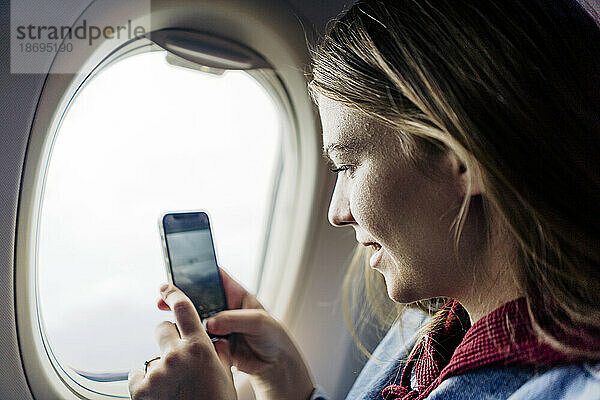 Frau fotografiert mit Smartphone im Flugzeug