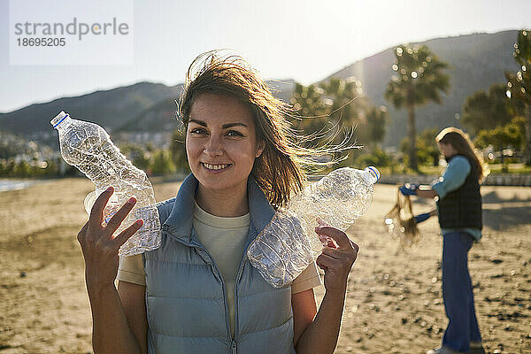 Lächelnde Frau hält zerknitterte Plastikflaschen am Strand