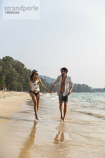 Paar hält sich an den Händen und geht am Strand in Ufernähe spazieren