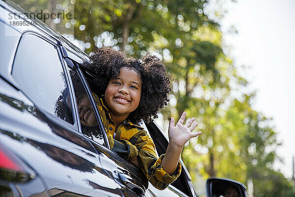 Lächelndes Mädchen lehnt und winkt vor dem Autofenster