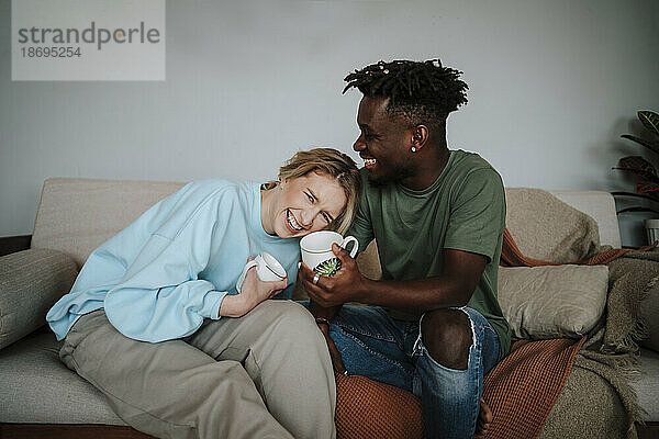 Glückliche Frau lacht mit Mann  der zu Hause eine Kaffeetasse hält